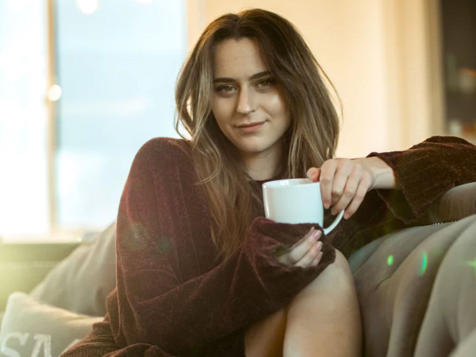 Auf Sofa sitzende junge Frau mit Teetasse